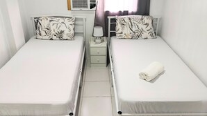 Une chambre double avec deux lits, chacun étant équipé d’un oreiller et d’une petite table de chevet avec une lampe.