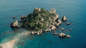 An aerial view of a small island with rocky terrain and a single building surrounded by clear blue waters.