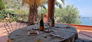 A round table set outdoors with a floral tablecloth, wine glasses, and a bottle of wine. - Private Villa Deluxe (Taormina)