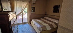 A bedroom with a bed, a dresser, a window with curtains, and a door leading to an outdoor area. - Private Villa Deluxe (Taormina)