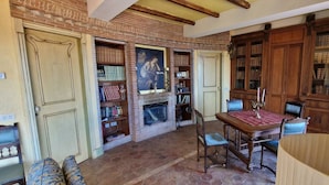 A library with bookshelves, a fireplace, a dining table, and a lamp. - Private Villa Deluxe (Taormina)