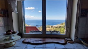 A room with a view of the sea through a large window, a small table with a fruit bowl, and a tiled floor. - Private Villa Deluxe (Taormina)