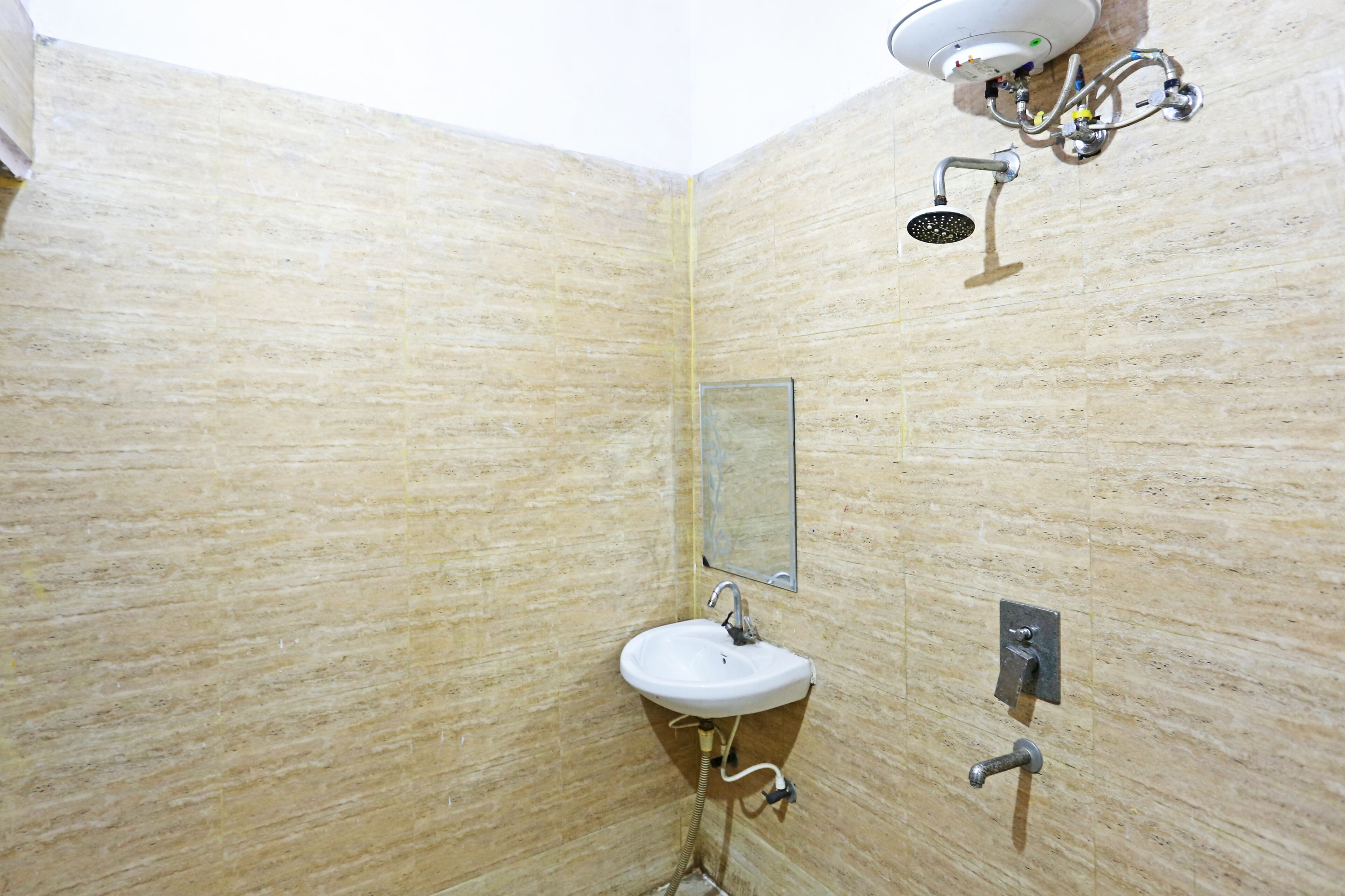 A bathroom with a beige tiled wall, a white sink, a mirror, and a shower head.