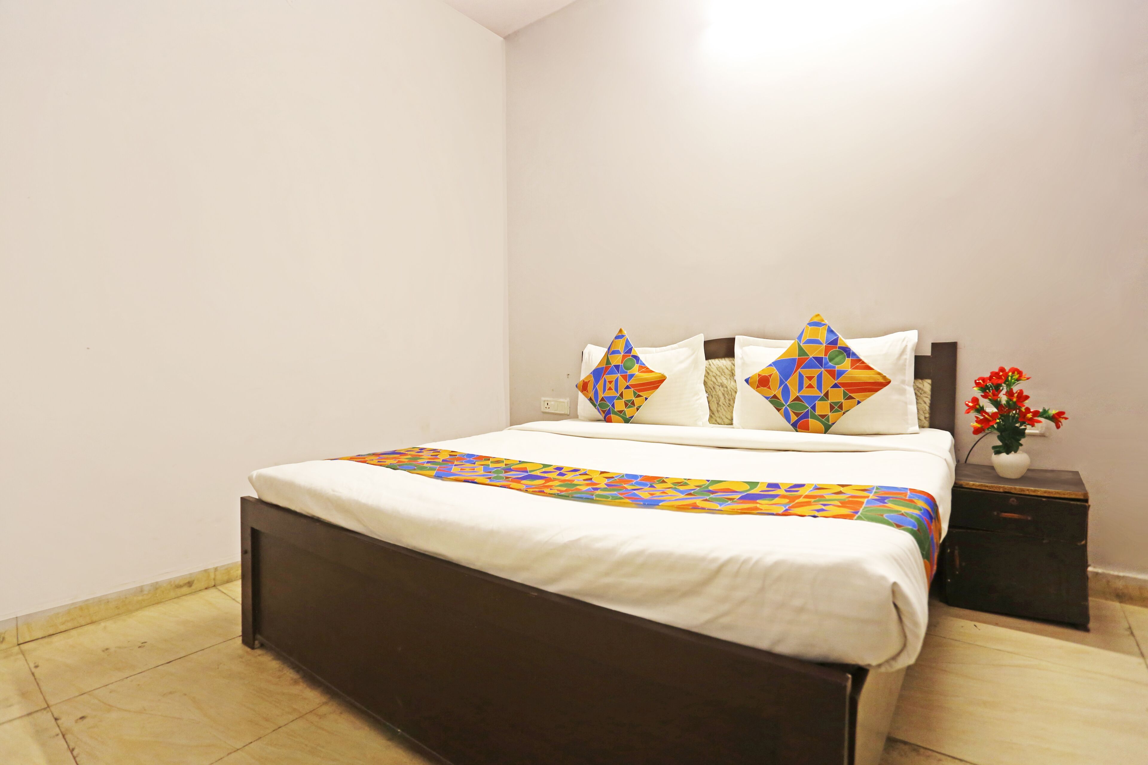 A neatly made bed with a colorful quilt, a dark wooden headboard, and a small bedside table with a vase of flowers.