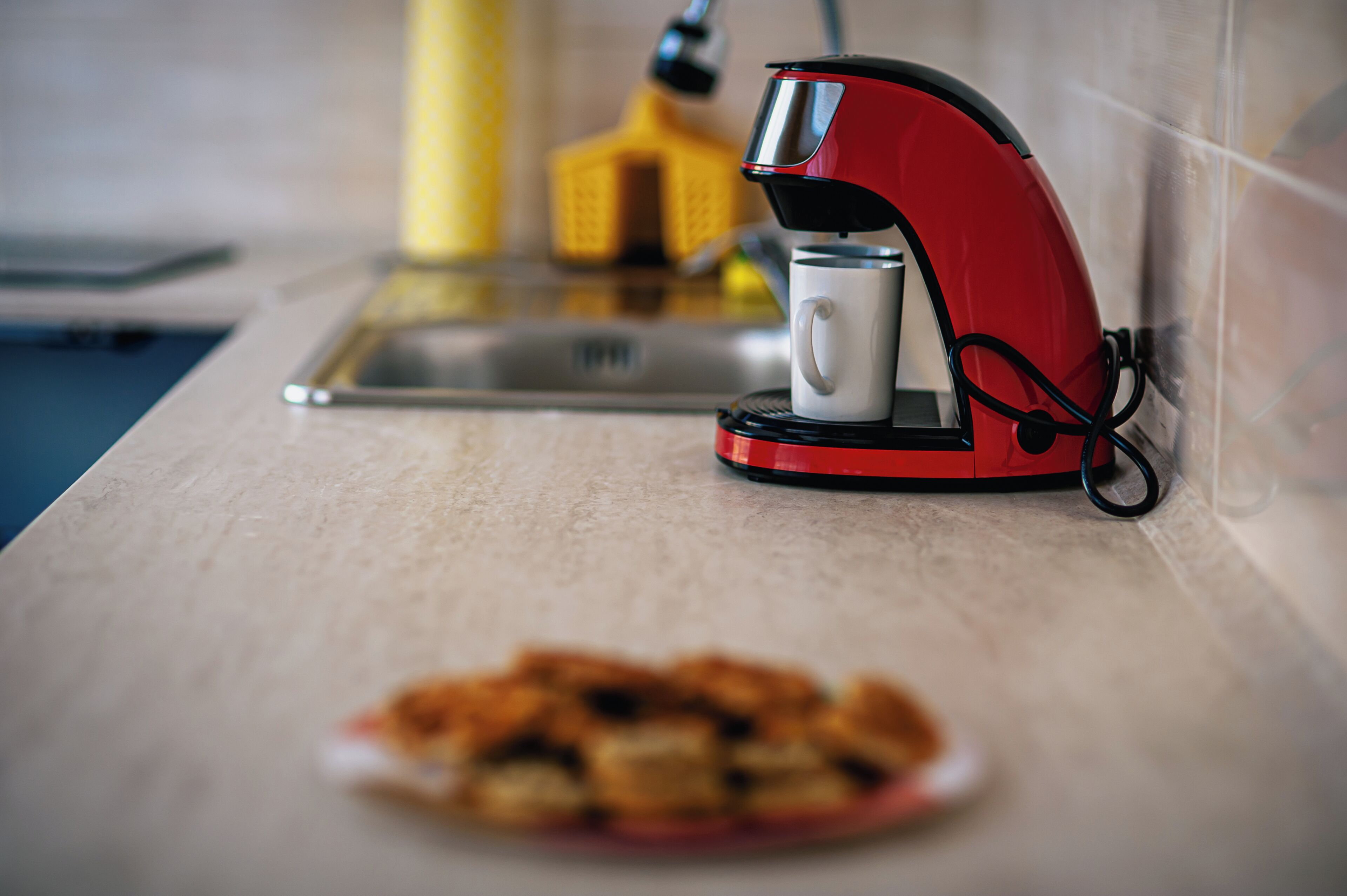 A red coffee maker on a kitchen counter with a plate of food in the foreground.