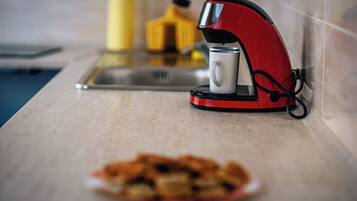A red coffee maker on a kitchen counter with a plate of food in the foreground.