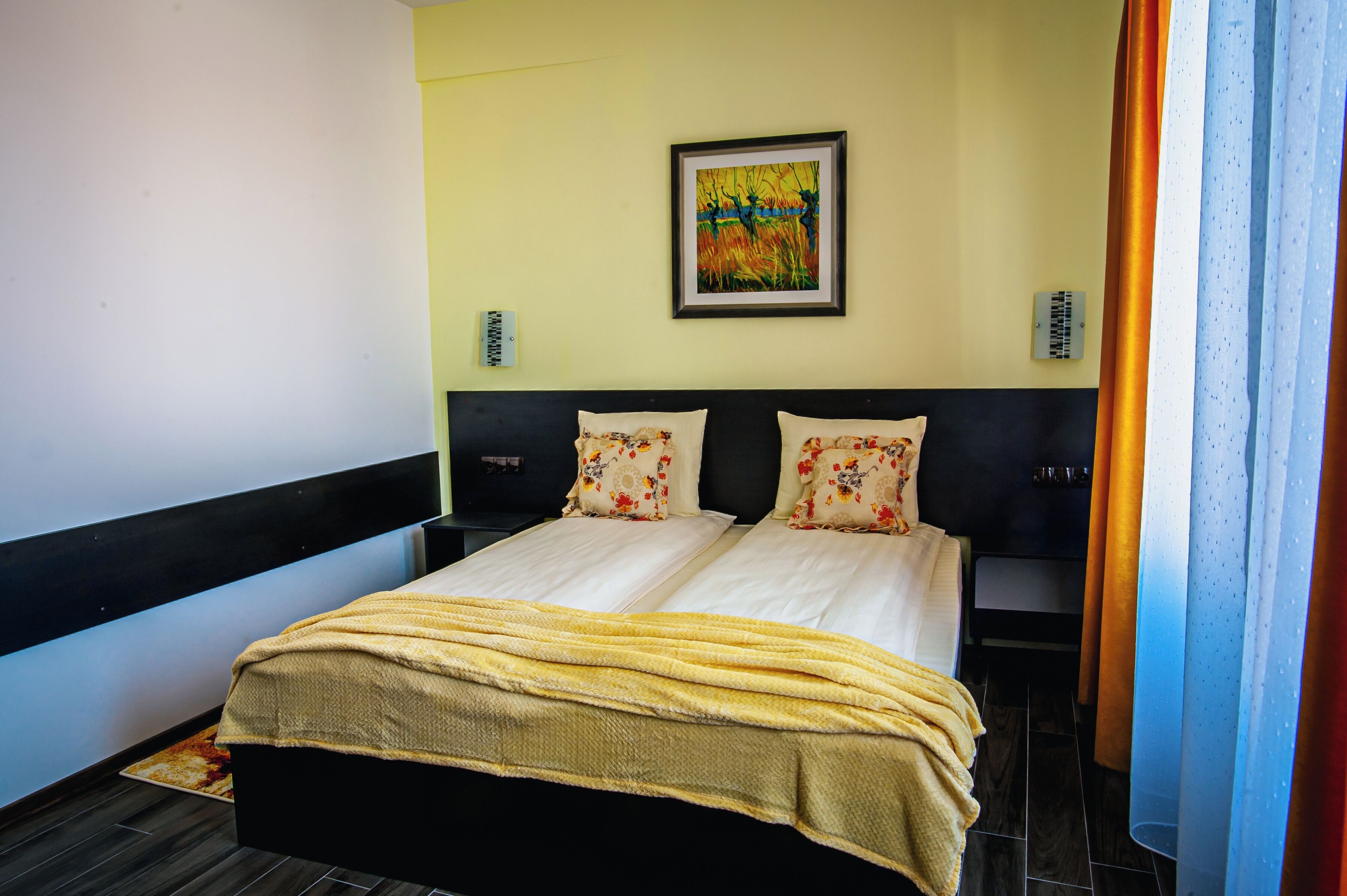 Un lit double avec une couverture jaune, un tableau encadré accroché au mur et une tête de lit noire.