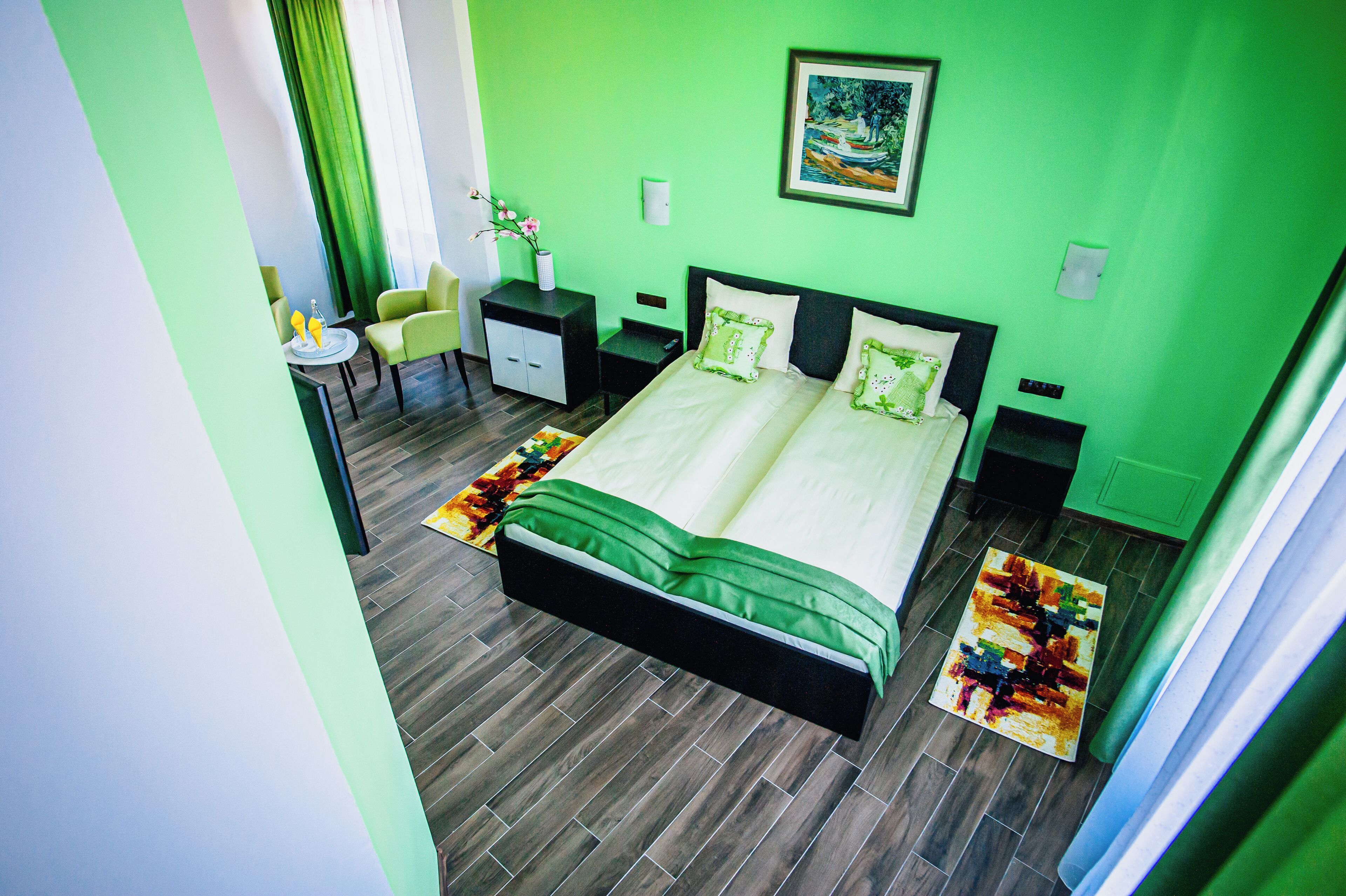 Une chambre d’hôtel avec un mur vert, un lit avec une literie verte, un petit bureau avec une chaise et un tableau accroché au mur.