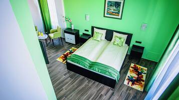 Une chambre d’hôtel avec un mur vert, un lit avec une literie verte, un petit bureau avec une chaise et un tableau accroché au mur.