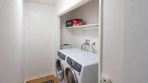 A laundry room with a washing machine and dryer, a shelf with a box, and a vent. - Mountain View, Near Yosemite & Bass Lake, EVC, BBQ (Oakhurst)