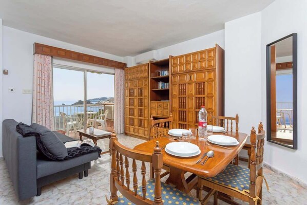 Un coin repas avec une table en bois dressée pour quatre personnes, un canapé et une bibliothèque.