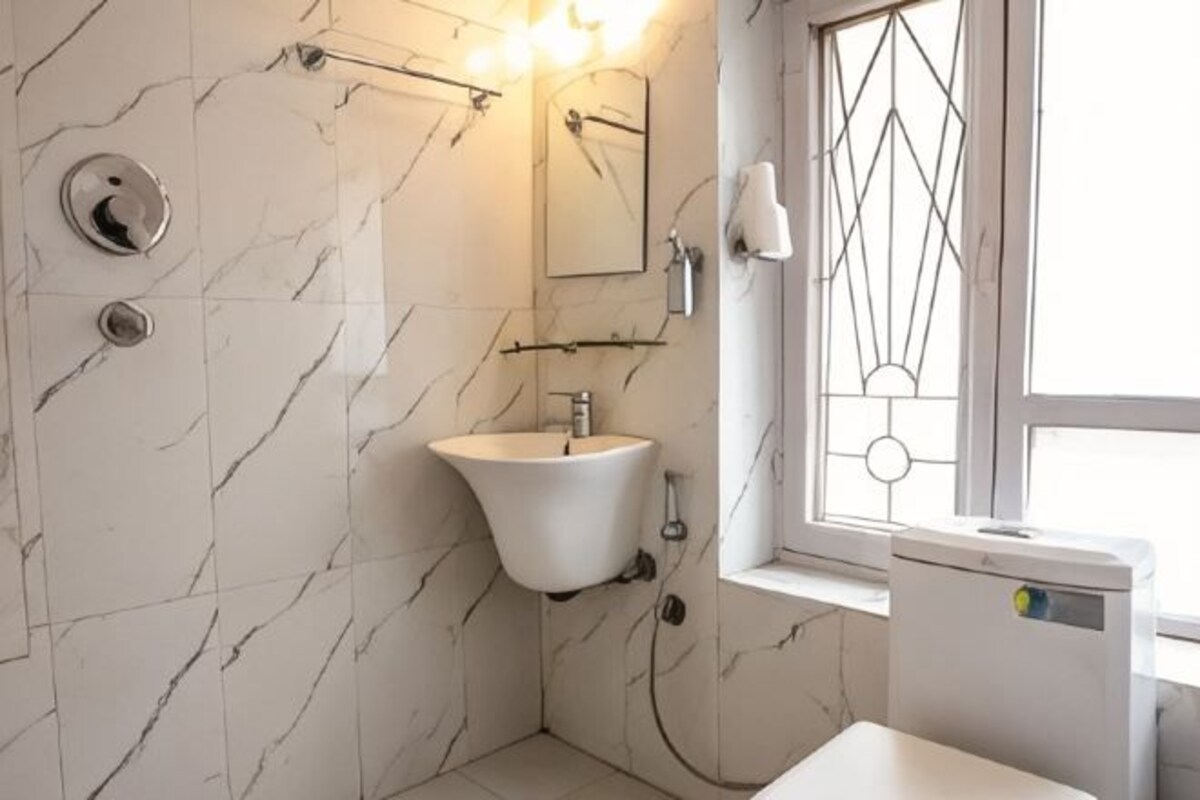 Un baño con pared de mármol, lavamanos, espejo, ventana con diseño geométrico e inodoro.