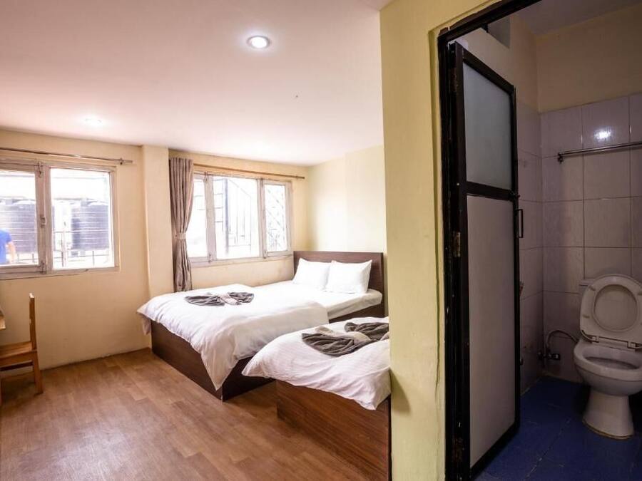 Una habitación con dos camas, una silla de madera, una ventana con cortinas y un baño con inodoro.