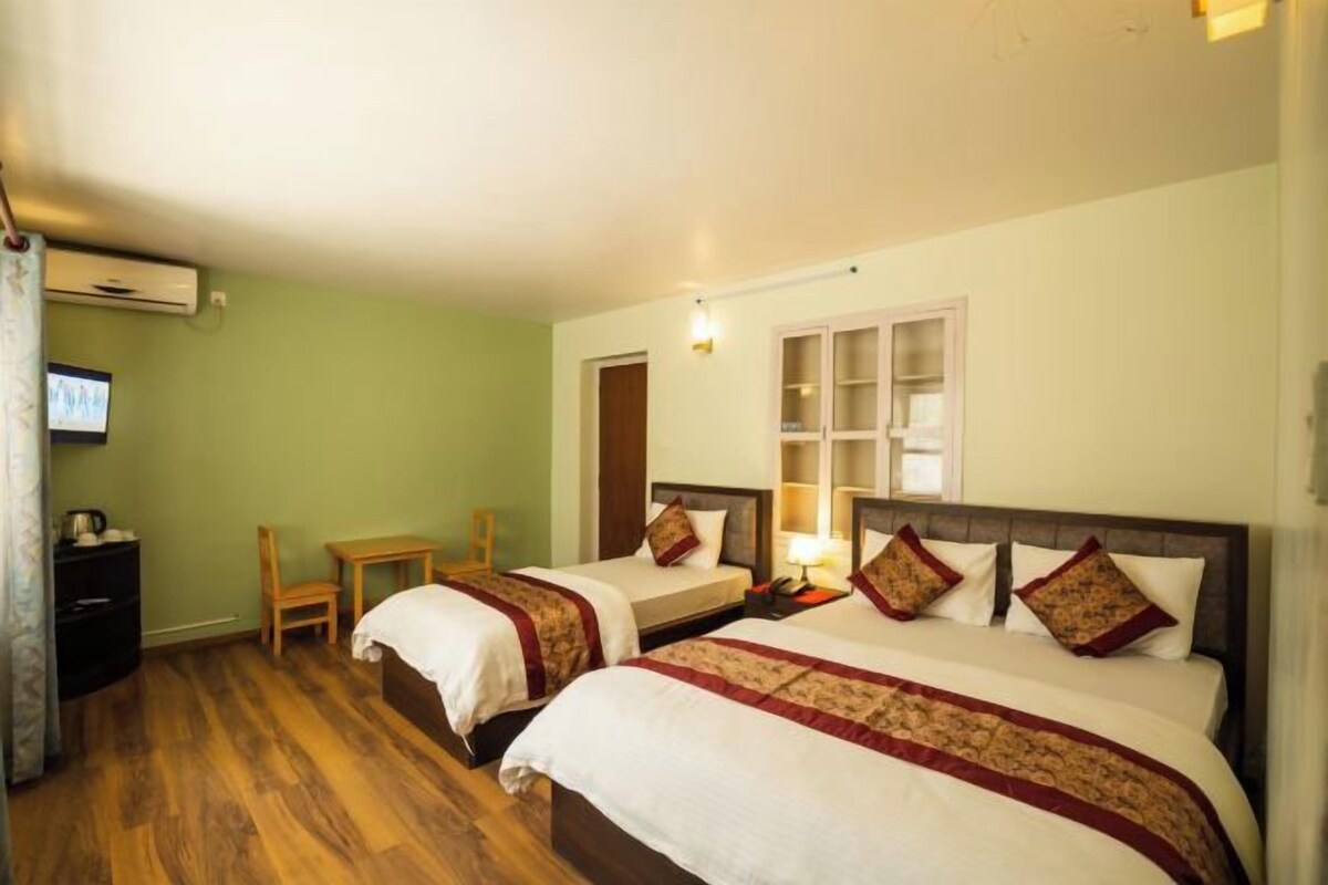 A hotel room with two beds, a wooden desk, a chair, a TV, and a window with a view.