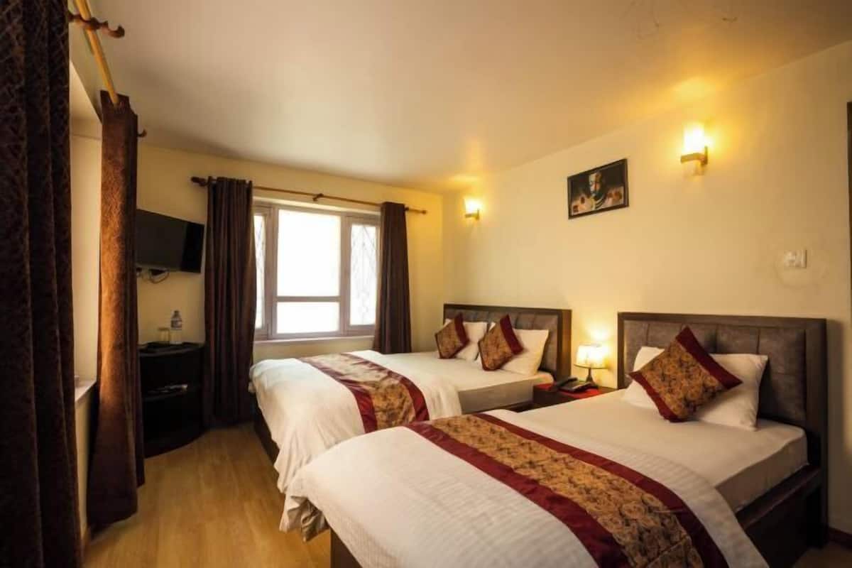 Une chambre d’hôtel avec deux lits, une télévision, une fenêtre avec des rideaux et des lampes fixées au mur.