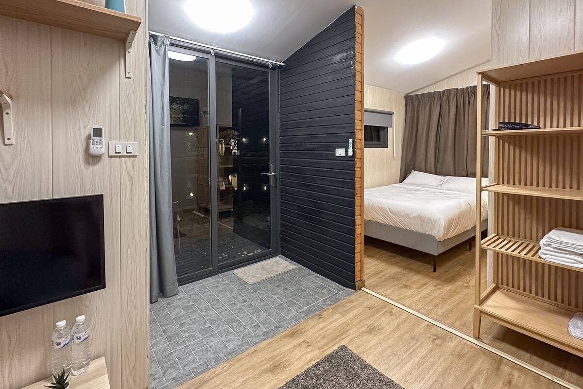 A modern hotel room with a sliding glass door, a bed, a TV, and a wooden wardrobe.
