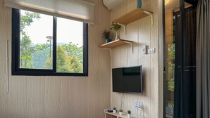A modern living room with a large window, wooden panel walls, a flat-screen TV, and a sliding glass door leading to an outdoor area. - Na Muen See  (Samoeng)