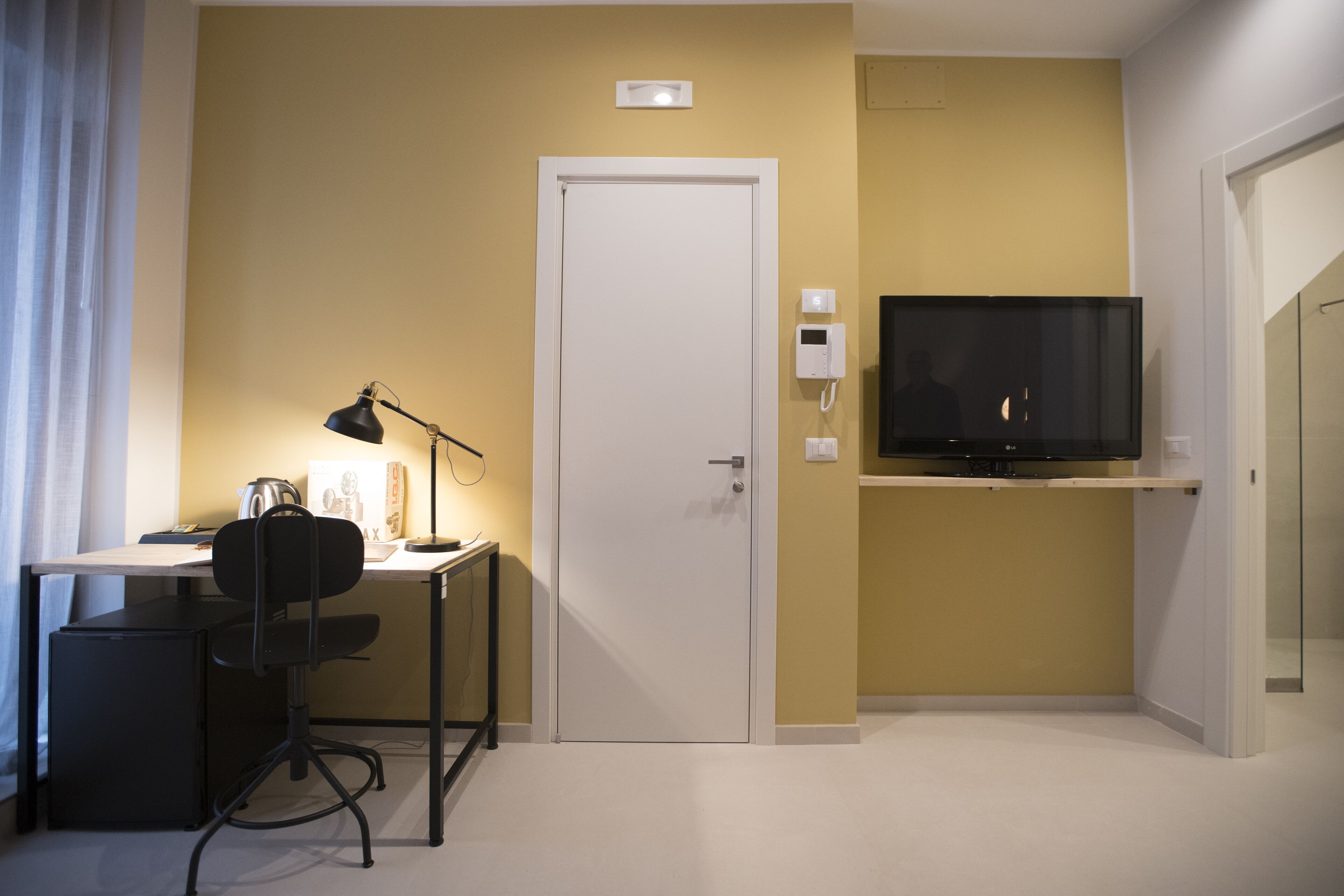 A compact hotel room with a desk, chair, and a television mounted on the wall.