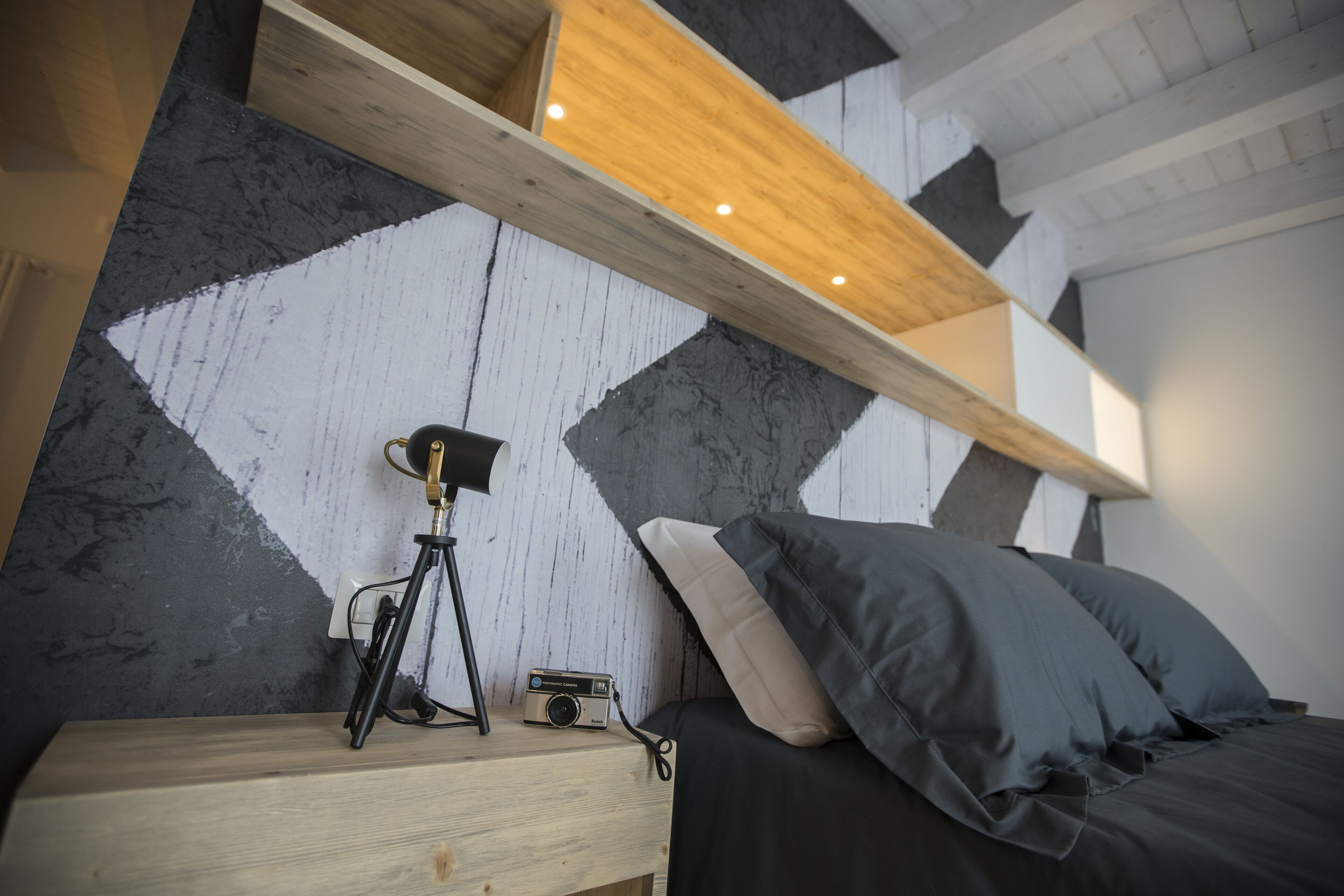 Una camera da letto con un letto, un comodino, una macchina fotografica e uno scaffale in legno.
