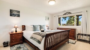 Ein Schlafzimmer mit Bett, Nachttischen, Kommode, Fenster mit Blick und Deckenleuchte.