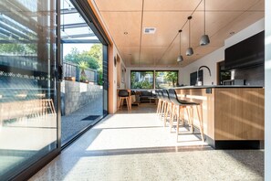 A modern kitchen with a bar area, large windows, and a seating area with a sofa and chairs.