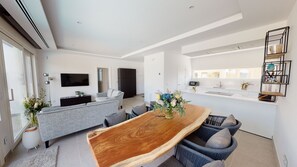 Ein modernes Wohnzimmer mit einem großen Esstisch aus Holz, grauen Sofas und einem flachbildfernseher an der Wand.