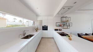 A modern kitchen with white cabinetry, a built-in oven, and a dining area with a wooden table and chairs.