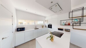 A modern kitchen with white cabinetry, a built-in oven, a microwave, and a large window providing natural light. - Villa Colibri by ON Travel (Oliva)