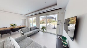 Un salon moderne avec un canapé, une table à manger et des chaises. Une porte-fenêtre coulissante donne accès à un espace piscine.