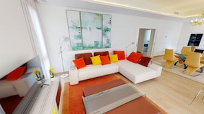 Uma sala de estar moderna com um sofá branco, almofadas laranja e amarelas, uma mesa de centro de vidro e um tapete vermelho. Há um quadro na parede e um abajur.