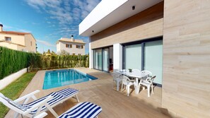 Ein moderner Poolbereich im Freien mit Liegestühlen, einem Esstisch und Blick auf angrenzende Häuser.