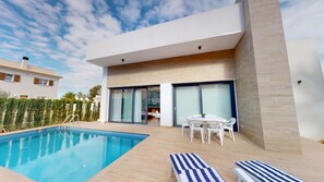 A modern poolside area with a swimming pool, lounge chairs, and a dining area with a table and chairs.