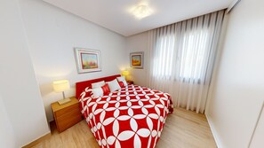 Ein Hotelzimmer mit einem großen Bett, zwei Nachttischen mit Lampen, einem Fenster mit durchsichtigen Vorhängen und zwei gerahmten Bildern an der Wand.