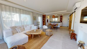 A modern living room with a white sofa, a wooden coffee table, and a dining area with a wooden table and chairs.