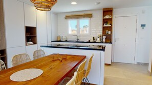 A modern kitchen with a wooden dining table, wicker chairs, and a built-in island with a sink. - Greenside oasis villa by ON Travel (Oliva)