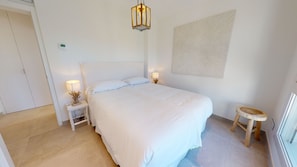 Ein Schlafzimmer mit einem großen Bett, zwei Nachttischen mit Lampen, einer Wandleuchte und einem kleinen Hocker.