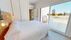 A bedroom with a large bed, a hanging light fixture, and a view of the outside balcony.
