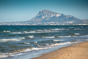 Une plage avec des vagues, une montagne en arrière-plan et un ciel dégagé.