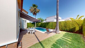 A pool area with a table and chairs, a covered patio, and a neatly trimmed lawn.