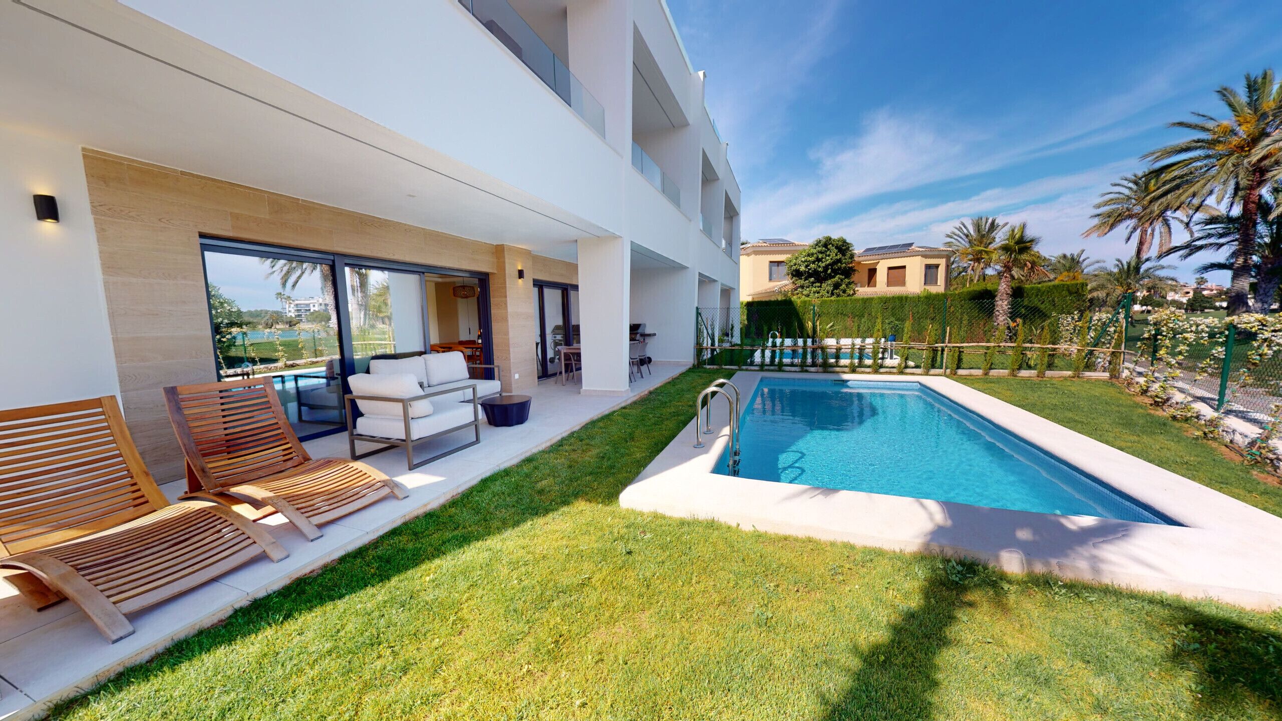 Un espace piscine extérieur moderne, doté d’une pelouse bien entretenue, d’un coin salon avec un canapé et des fauteuils, et offrant une vue dégagée sur la piscine.
