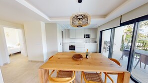 Une cuisine moderne avec des meubles blancs, une table à manger entourée de quatre chaises et une grande fenêtre donnant sur un balcon.