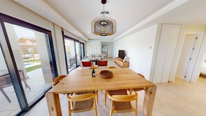 Un vaste espace de vie comprenant une table à manger en bois, des chaises en osier et un lustre moderne.