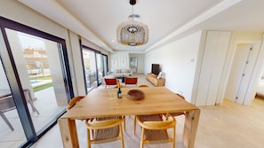 Ein großzügiger Wohnbereich mit einem großen Esstisch aus Holz, Korbstühlen, einer modernen Chandelierleuchtre und Blick auf einen Pool durch große Glasschiebetüren.