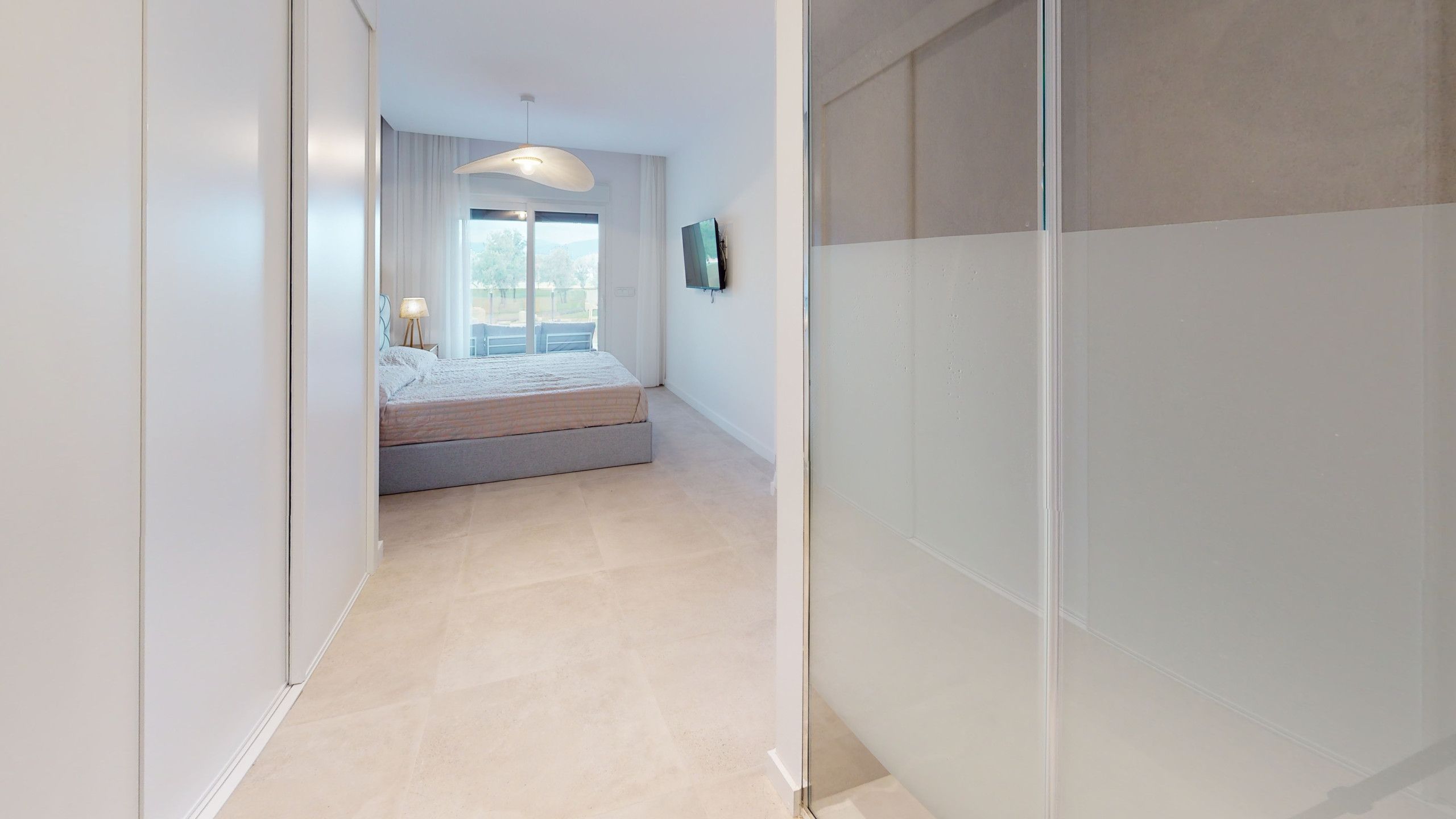 A modern bedroom with a bed, a bedside table, a lamp, and a window with a view.