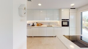 A modern kitchen with white cabinetry, a built-in oven, and a window providing a view of the outdoors. - Lirio by ON Travel (Oliva)