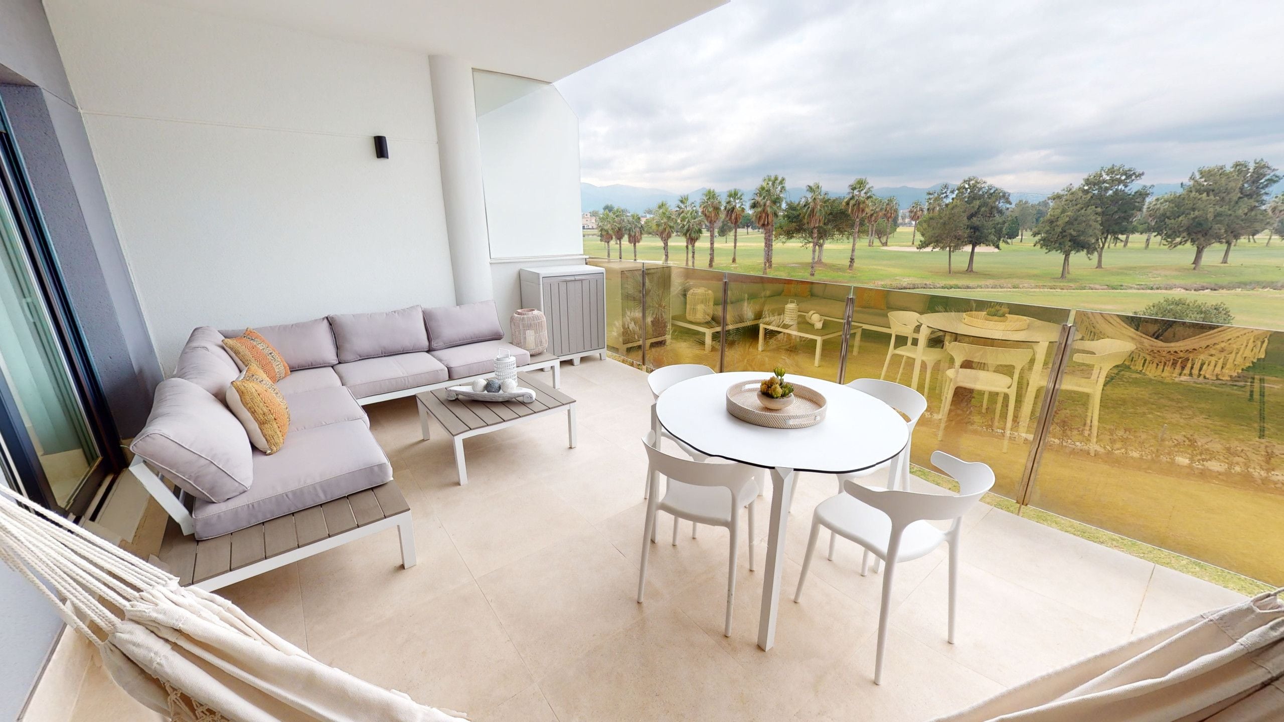 Een balkon met een bank, salontafel en eettafel met stoelen, met uitzicht op een golfbaan.