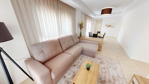 Een moderne woonkamer met een hoekbank, een houten salontafel en een eethoek met een tafel en stoelen.