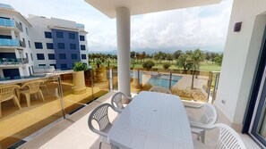 Een balkon met een tafel en stoelen, een zwembad en uitzicht op een golfbaan.