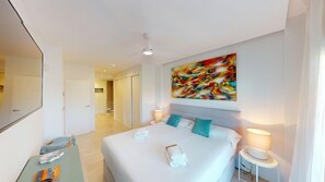 Ein Hotelzimmer mit Bett, Schreibtisch, Stuhl, Deckenventilator, einem Gemälde und einem Nachttisch mit Lampe.