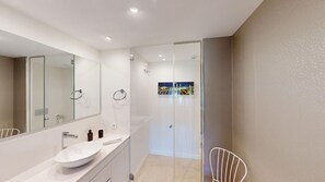 A modern bathroom with a large mirror, a white sink, and a glass shower enclosure. - Petunia by ON Travel (Oliva)